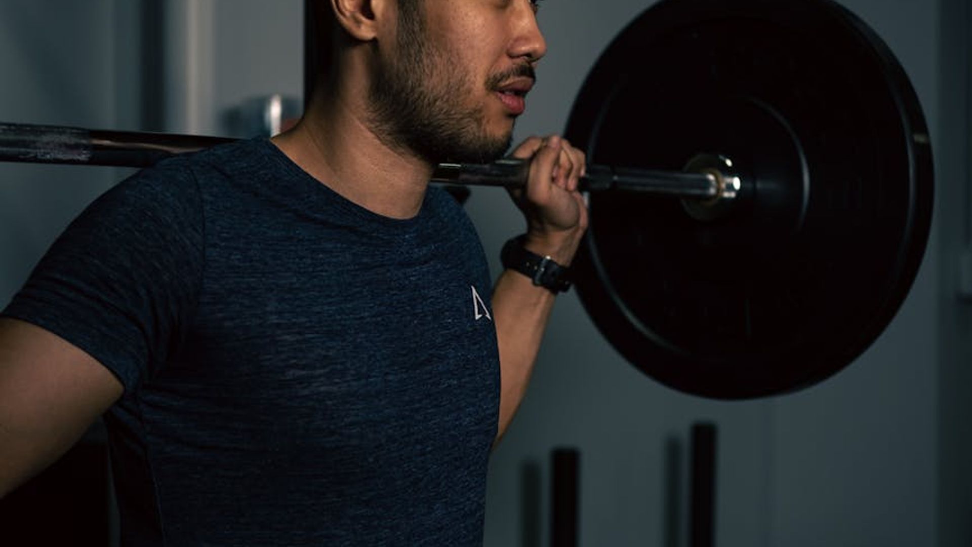 Man in a focused stance during a strength workout in a dark gym.